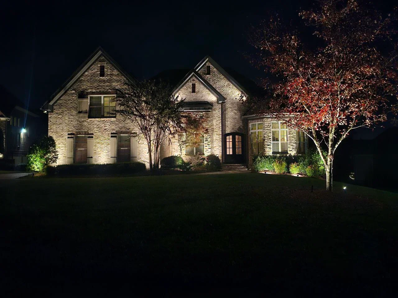 Stone home at night with professional uplighting on facade and landscape accent lighting