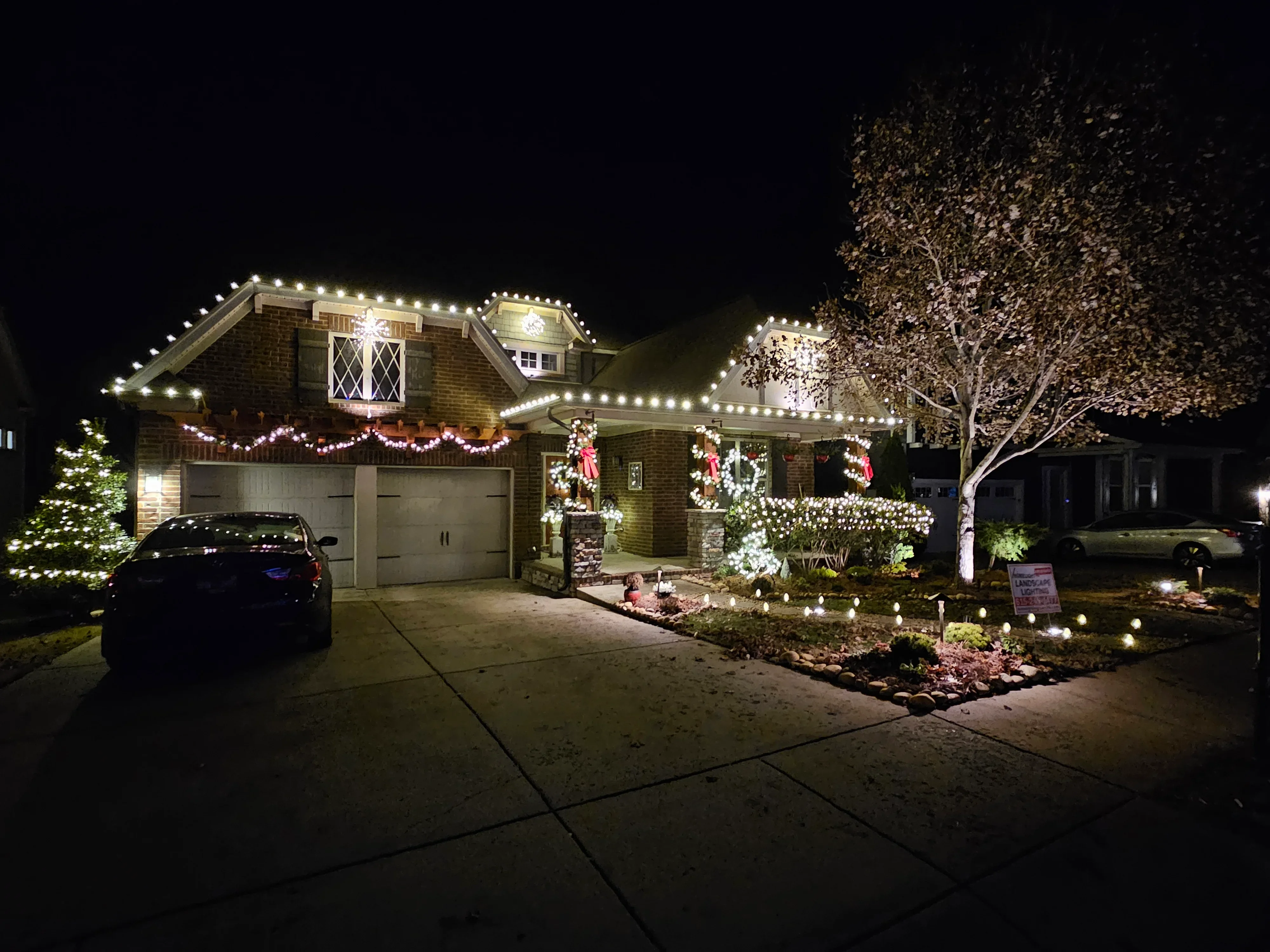 Brick home at night with white roofline lights, holiday wreaths, and landscape uplighting