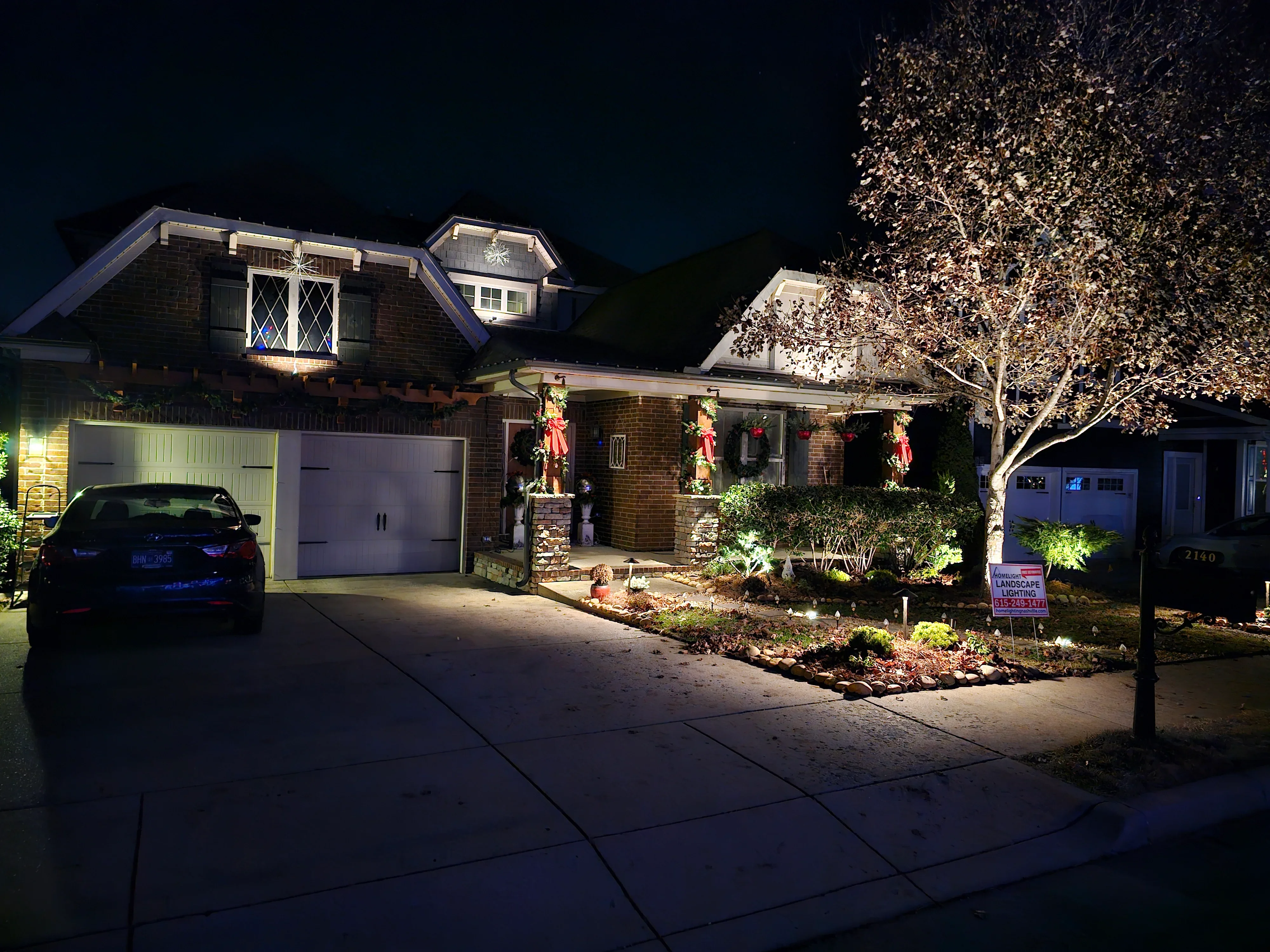 Brick home at night with uplighting on trees, architectural accent lights, and landscape lighting