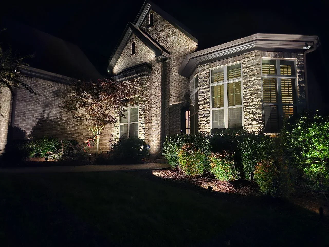 Nighttime view of brick home with architectural uplighting on facade and landscape accent lighting