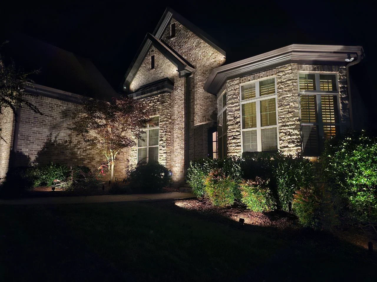 Night view of stone home with architectural uplighting on facade and landscape accent lighting