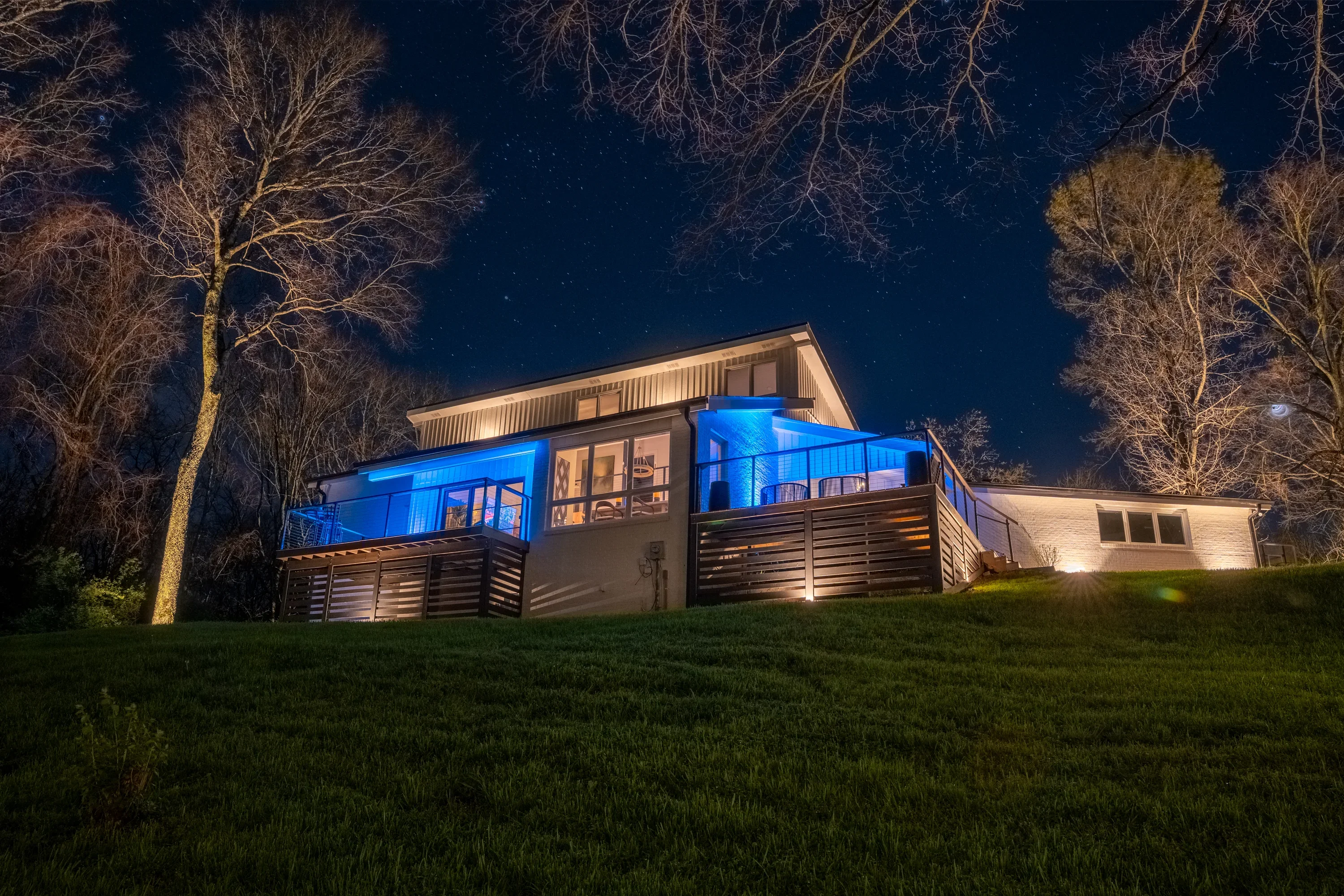 Modern home at night with blue deck lighting and warm facade uplighting