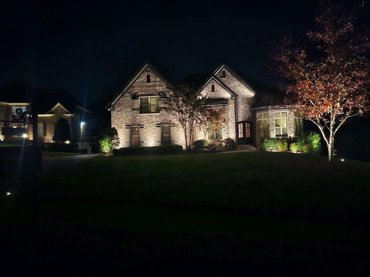 Stone home at night with warm uplighting on facade, landscaping, and trees