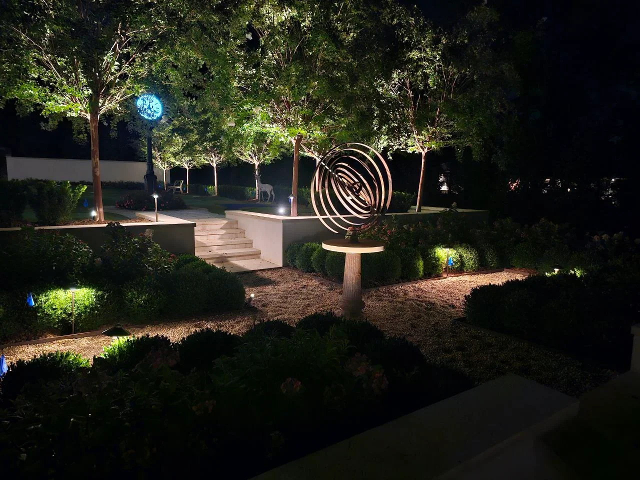 Nighttime garden with uplighting on trees, spiral sculpture, and pathway lights