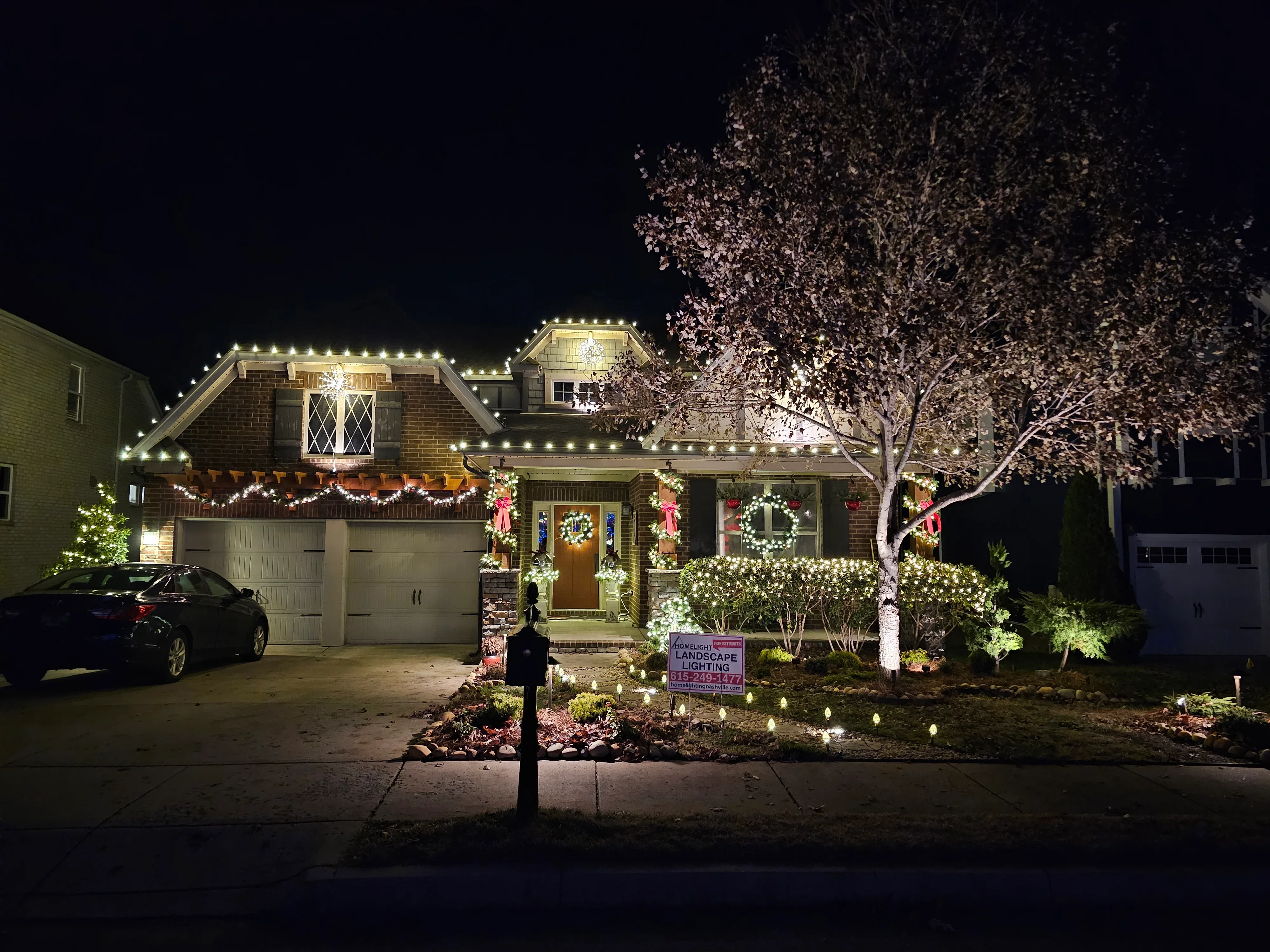Two-story home at night with professional holiday lighting on roofline, trees, and landscaping
