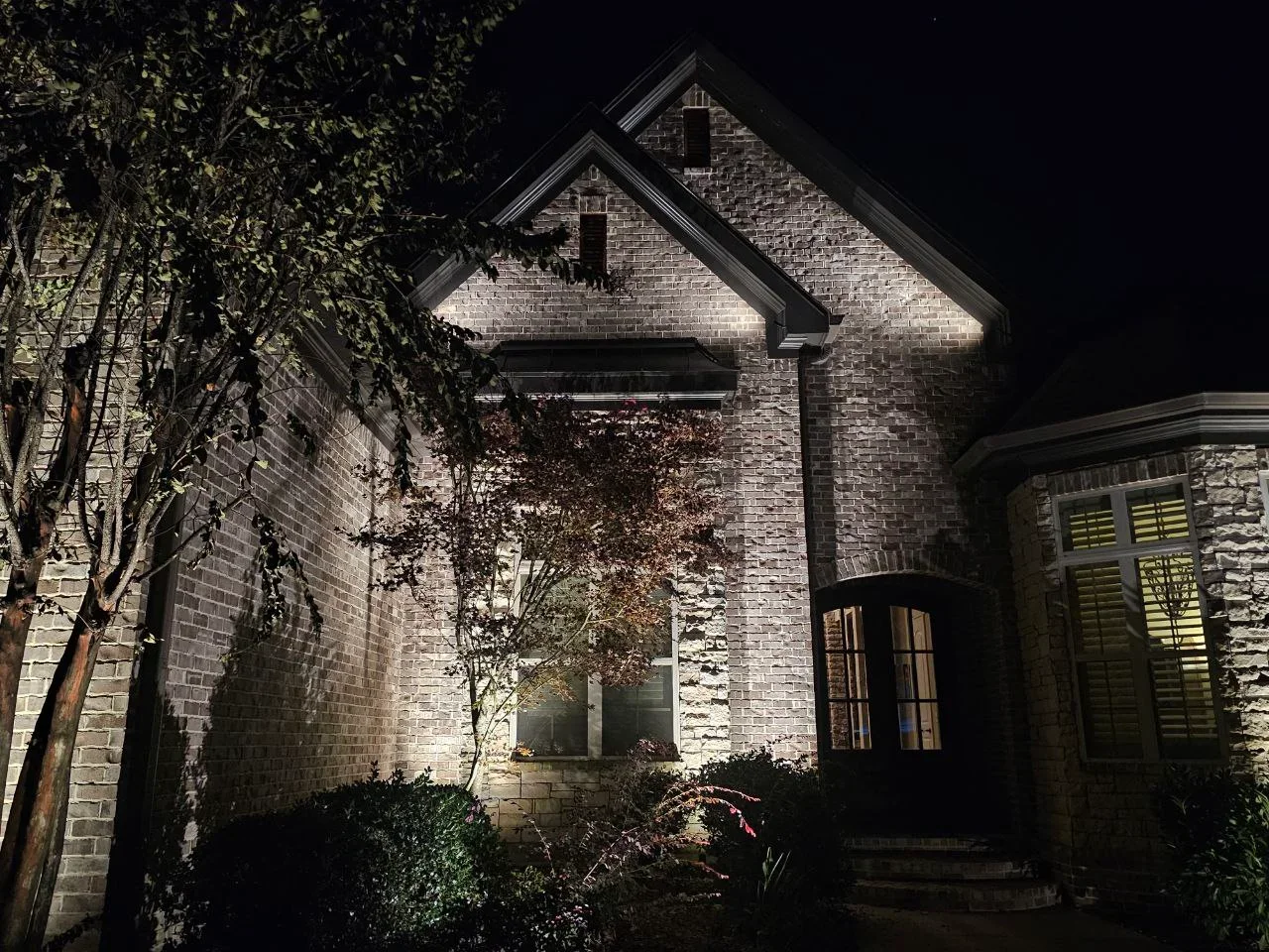 Night view of brick home with warm uplighting on facade and gable rooflines