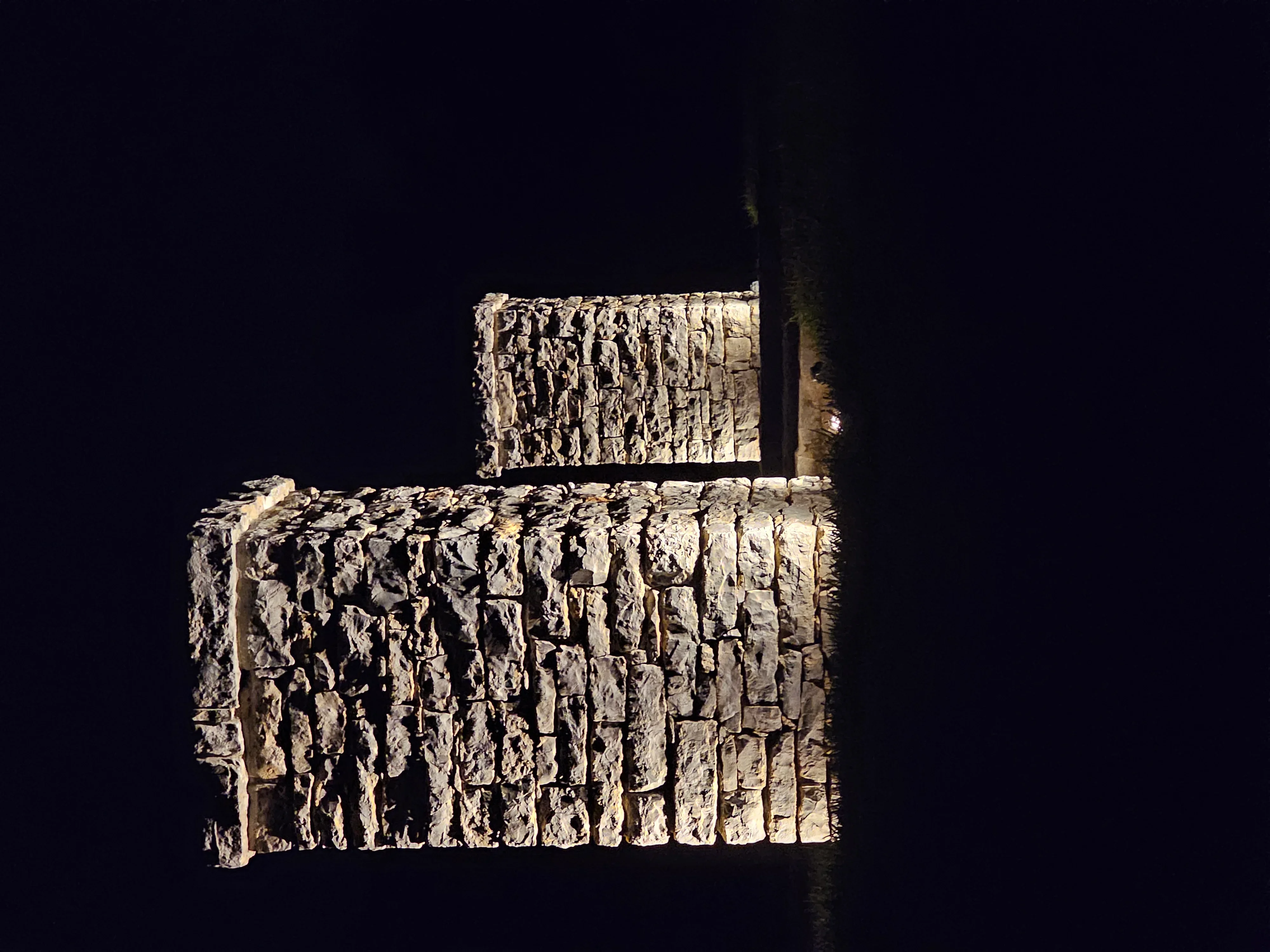 Warm uplighting on stacked stone wall at night, creating dramatic shadows and texture emphasis