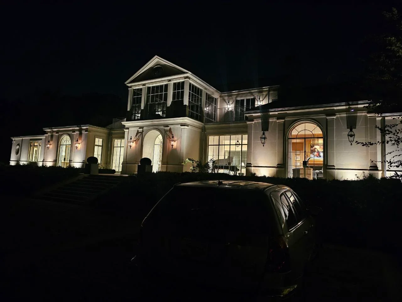 Nighttime exterior lighting on white contemporary home with cupola and arched windows