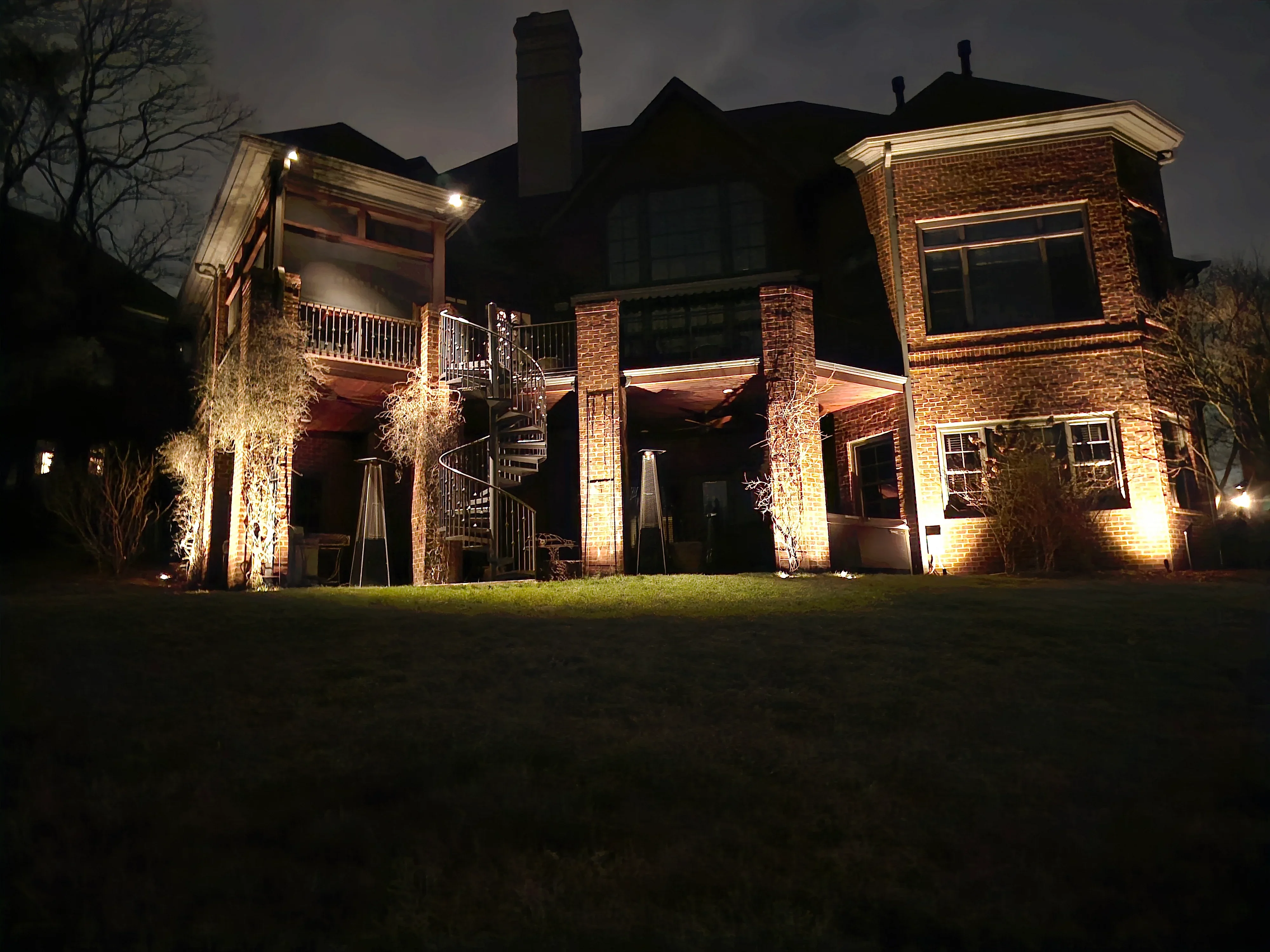 Brick estate home at night with warm uplighting on facade, columns, and landscaping