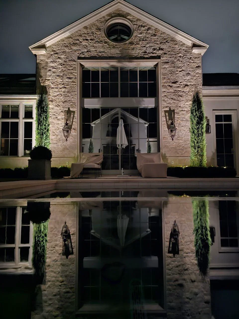 Stone home exterior at night with architectural accent lighting on facade, entry, and landscape features