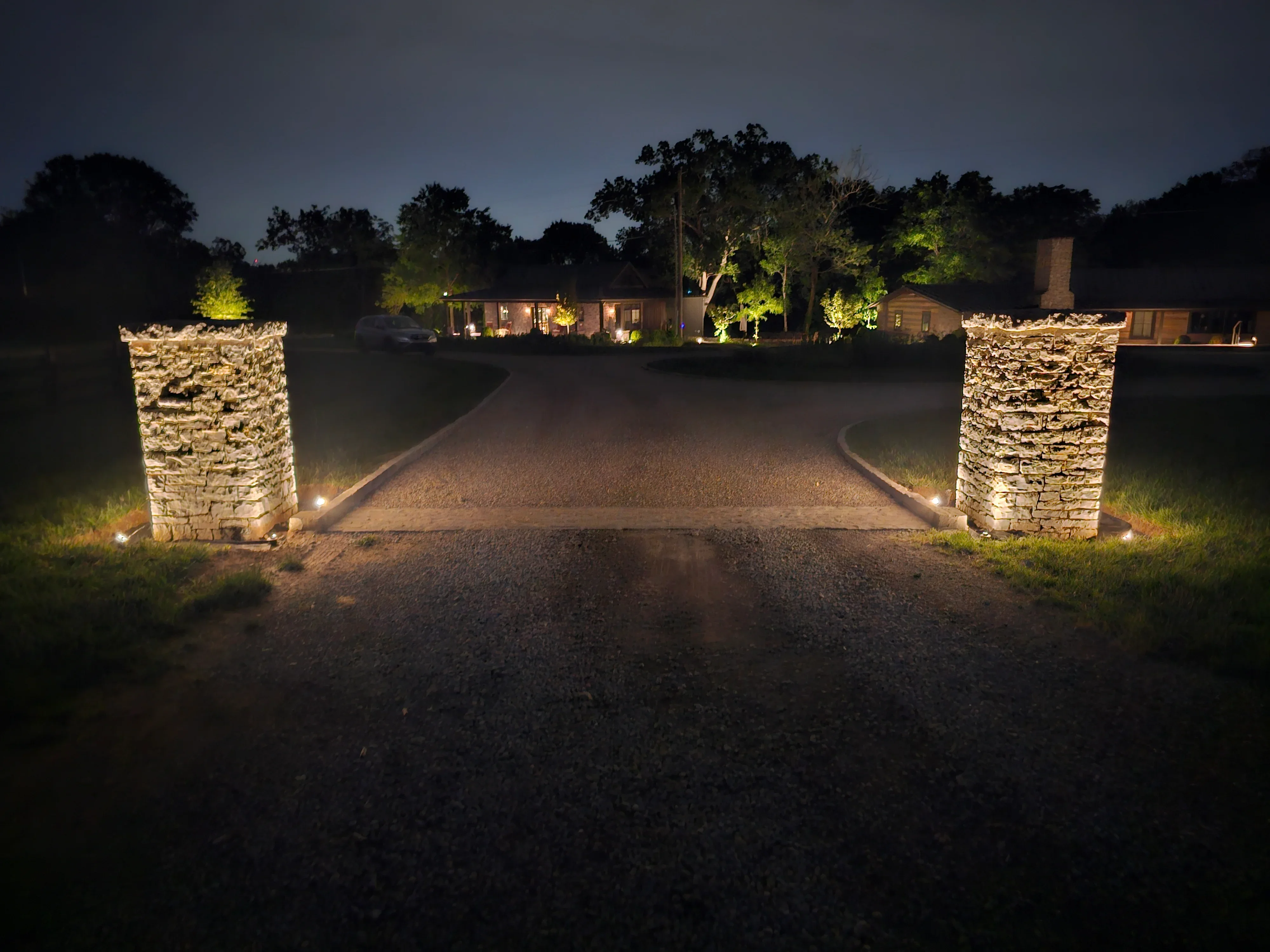 A Franklin, TN residential property at night with low-voltage LED pathway lights lining the front walkway and uplights illuminating mature trees along the facade. The home's architectural details are visible from the street under warm, evenly distributed outdoor lighting installed by Homelight Nashville.